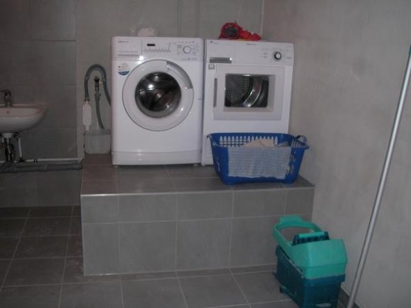 Extra Podest für Waschmaschine und Trockner mit Abstellfläche für Wäschekörbe davor.
