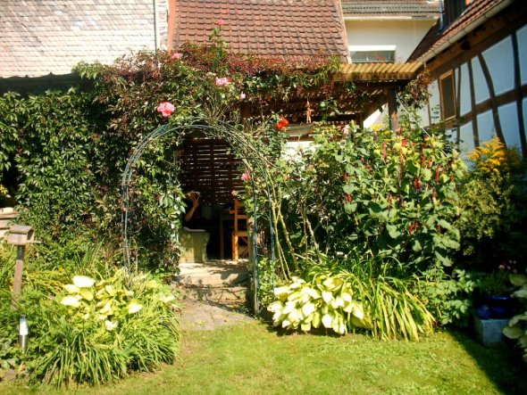 Blick durch den Rosenbogen auf den Sitzplatz, wie er vorher war - ohne Holz